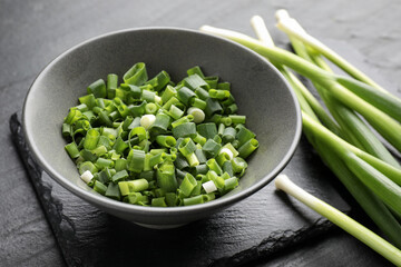 Whole and cut fresh green onions on black table, closeup