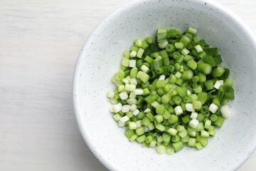 Cut fresh green onions in bowl on light wooden table, top view. Space for text
