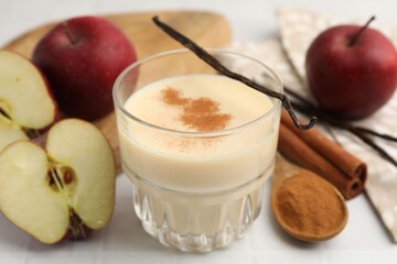 Delicious protein shake in glass, apples, cinnamon and vanilla pods on white table, closeup