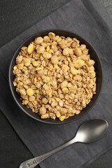 Tasty granola in bowl and spoon on black table, flat lay