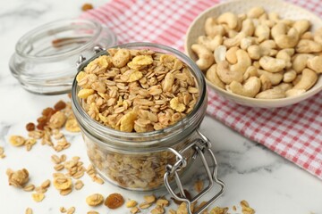 Tasty granola in glass jar on white marble table, closeup