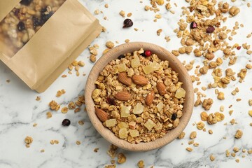 Naklejka premium Tasty granola with dried fruits and nuts in bowl and paper bag on white marble table, flat lay