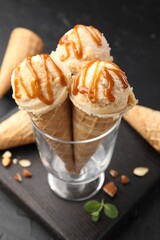 Tasty ice cream with caramel sauce in waffle cones on black table, closeup