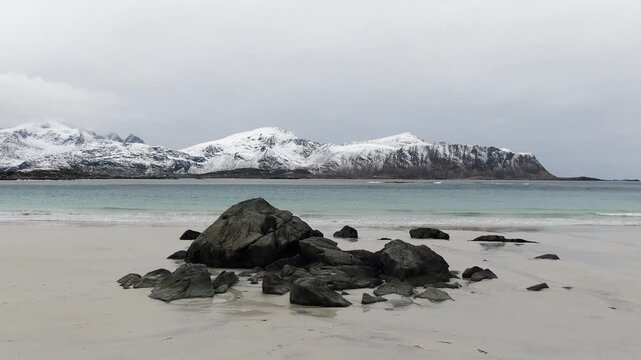 A drone view over Ramberg Beach in the Lofoten Islands reveals icy winter scenery, with snow-covered shores and striking turquoise-blue water under cold Arctic light.