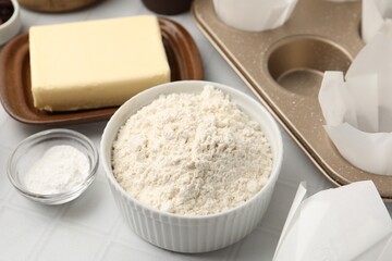 Ingredients for making muffins and cupcake tray on white tiled table, closeup
