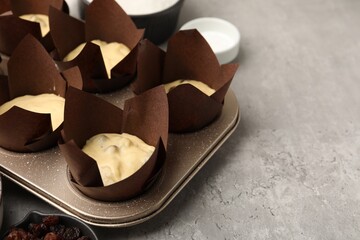 Making muffins. Cupcake tray with dough and other different ingredients on grey table, closeup. Space for text