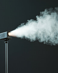 White smoke blowing from black machine on stand creating cinematic fog effect against dark background showing mysterious atmosphere