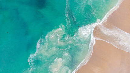 Aerial view of the turquoise sea meeting the sandy shore in a dance of white foam and golden hues at Hazards Beach, Tasmania, Australia.