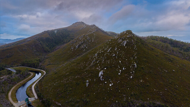 Aerial view of rugged peaks and a winding canal carve through the landscape under a cloudy sky near Lake Dobson Road, Mount Field National Park, Tasmania, Australia.