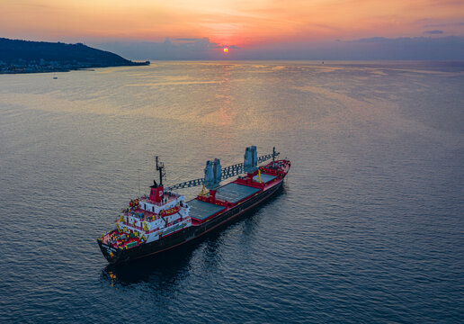 Aerial view of a cargo ship sailing on the open sea towards the horizon beneath a vibrant sunset sky, Haifa, Israel.