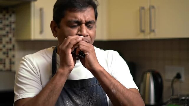 Man plays harmonica in kitchen, wearing apron, indoor, musical, musician.