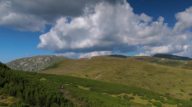 Bucegi Mountains 180 degree aerial panorama over the alpine plateau, revealing Scara, Omu, Gavanele, Costila and Piatra Arsa peaks beneath dramatic fast-moving summer clouds and deep blue sky, Romania
