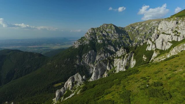 Bucegi Mountains aerial reveal over Gutanu, Lancia and Scara peaks, opening to the dramatic Gaura Valley with steep limestone cliffs, erosion towers and dense Pinus mugo slopes, Romania