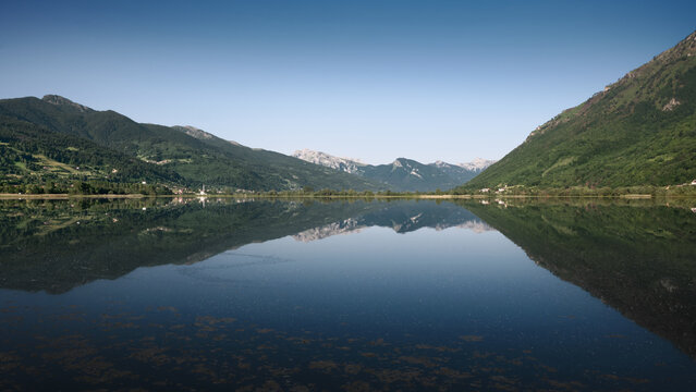 Calm mountain lake with still water and perfect mirror reflection of green hills and distant peaks under clear blue sky, peaceful nature scene for travel and outdoor concepts. Plav, Montenegro