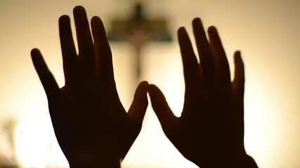 Hands raised in prayer towards a cross, a silhouette of faith and devotion, emphasizing spirituality and belief