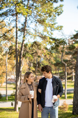 Couple enjoys a sunny afternoon walk in the park while holding coffee cups