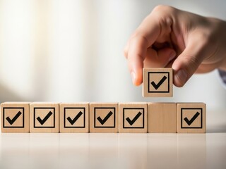 A hand placing a wooden block with a checkmark on top of a row of blocks with checkmarks on a table with a blurred white background