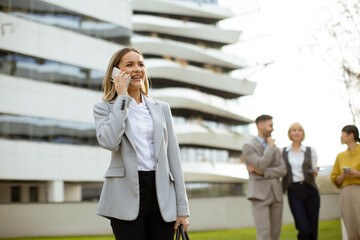 Businesswoman smiles while talking on phone outside modern office building during workday