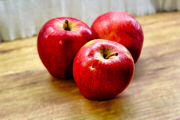 Three red apples are sitting on a wooden table