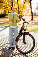 Korean woman smiles while talking on the phone next to her bicycle on a sunny autumn day
