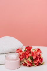 Pink face cream jar with flowers and towels on coral background. High quality photo