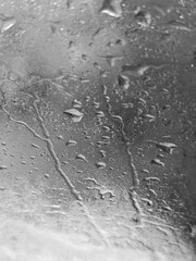 Raindrops cascade down a window surface in an artistic grayscale display, capturing the essence of the weather