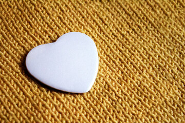 Obraz premium Heart Badge Mockup. White heart badge on textured knitted fabric, ideal for romantic or custom designs. A blank heart-shaped pin resting on warm textile, perfect for personal artwork display