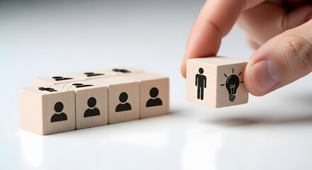 Hand placing a wooden cube with a person and lightbulb icon next to a row of team members