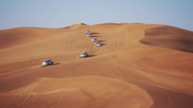 Convoy of trucks drive at golden desert dunes of Dubai in the United Arab Emirates
