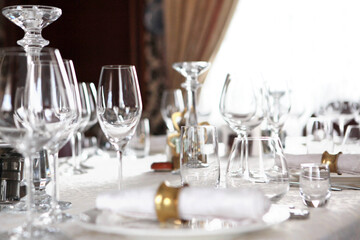Festive table setting in the interior. Wine glasses and plates on the table. A white tablecloth. A cotton serving napkin with a yellow metal ring. The concept of the holiday.