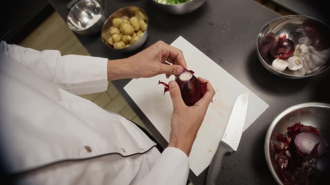 POV shot of male chef peeling red onion while cooking fresh salad on workbench in commercial kitchen, soft vignette effect