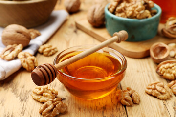Delicious honey in glass bowl, dipper and walnuts on wooden table, closeup