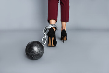 Businesswoman with metal ball and chain on her leg against grey background, closeup
