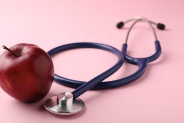 Ripe apple and stethoscope on pink background, closeup