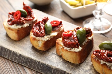 Delicious bruschettas with cream cheese, sun-dried tomatoes, chili pepper and green olives on table, closeup