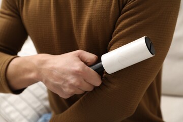 Man cleaning clothes with lint roller at home, closeup