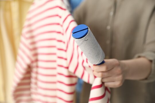 Woman cleaning sweatshirt with lint roller at home, closeup