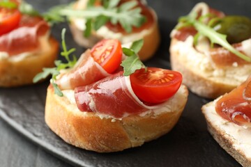 Delicious bruschettas with cream cheese, prosciutto, green olives, tomatoes and arugula on table, closeup