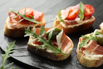 Delicious bruschettas with cream cheese, prosciutto, green olives, tomatoes and arugula on table, closeup
