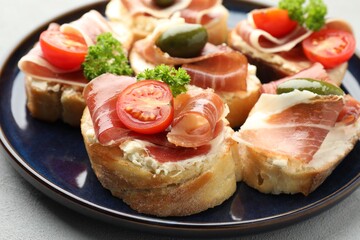 Delicious bruschettas with cream cheese, prosciutto, green olives, tomatoes and parsley on table, closeup