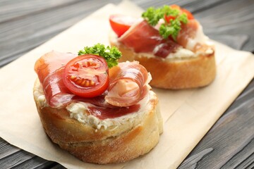 Delicious bruschettas with cream cheese, prosciutto, tomatoes and parsley on wooden table, closeup