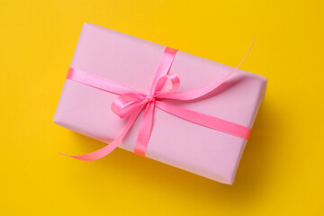 Beautiful wrapped gift with bow on yellow background, top view