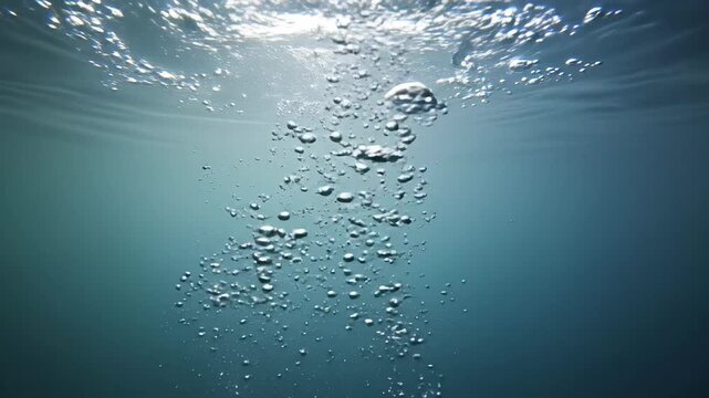 Sunlit underwater scene with rising air bubbles and gentle ripples.