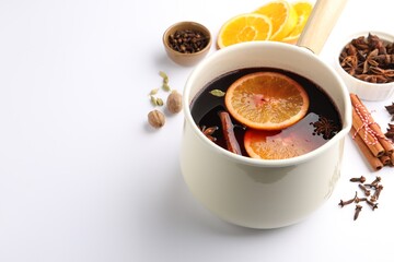 Tasty mulled wine in pot and ingredients on white table, closeup. Space for text