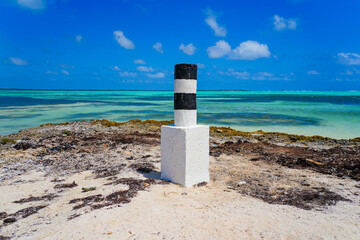 Striped navigation marker on Sorobon Beach in Lac Bay, a tropical lagoon with shallow turquoise...