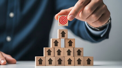 Reaching the Goal: A person strategically places a wooden block with a target on top of the pyramid, symbolizing the process of achieving goals.