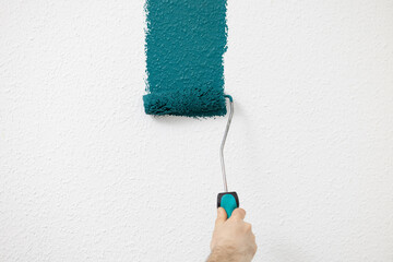 Hand holding paint roller applying teal paint on textured wall, showcasing home improvement and creative interior design concepts. free space