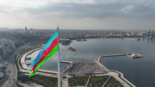 Majestic aerial drone view of the national flag of Azerbaijan waving over Baku cityscape and Caspian Sea bay