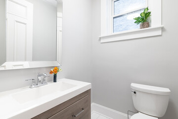 A clean and modern bathroom featuring a wood vanity with a sink, faucet, and mirror, adjacent to a toilet.