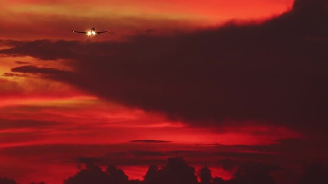 Silhouette of aircraft flying in orange sunset sky with clouds illuminated by setting sun. Gorgeous cloudscape with airplane. Flight of plane with flashing lights at sundown. Camera stays still.